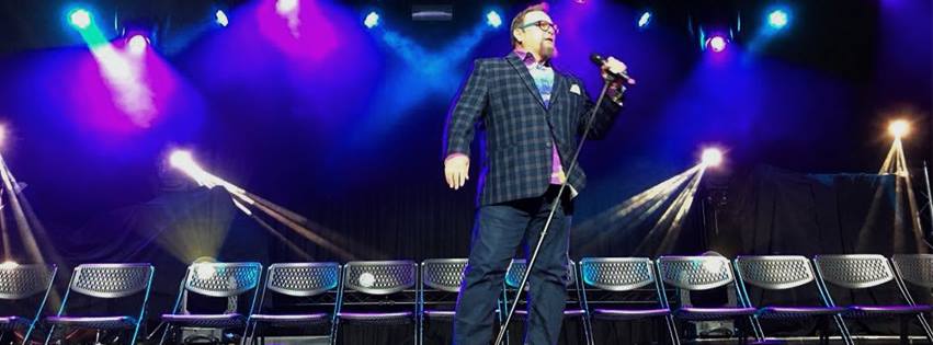 Comedy Hypnotist CJ Johnson on stage with empty chairs and full stage lights